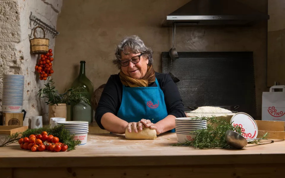 Una nonna con il grembiule impasta la pasta in una cucina di pietra