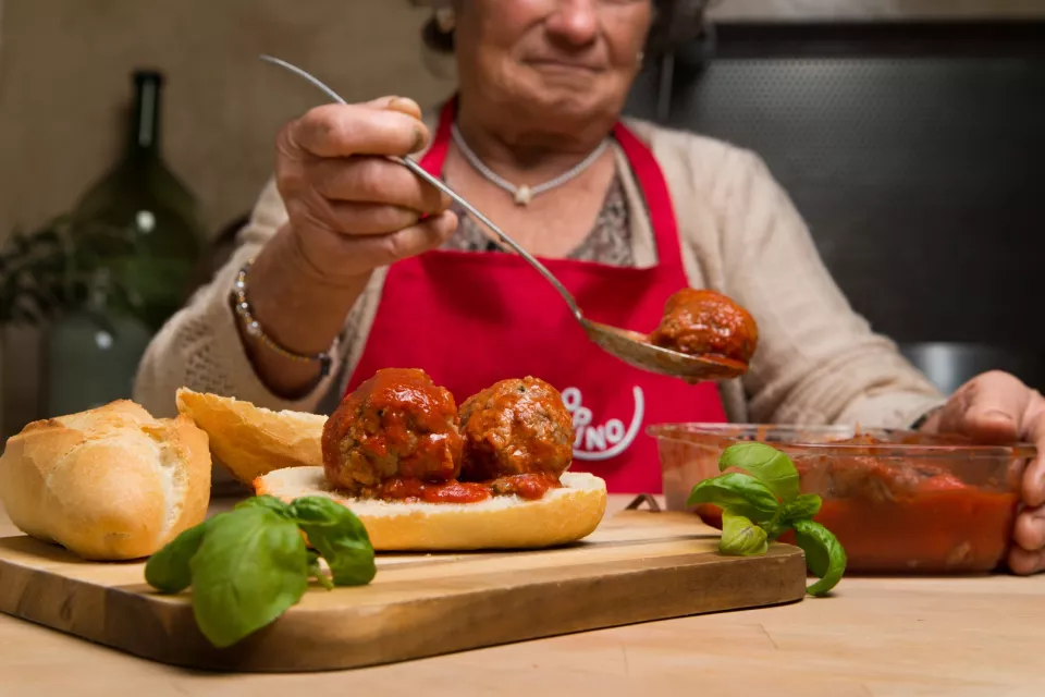 Una nonna versa il sugo sulle polpette dentro un panino